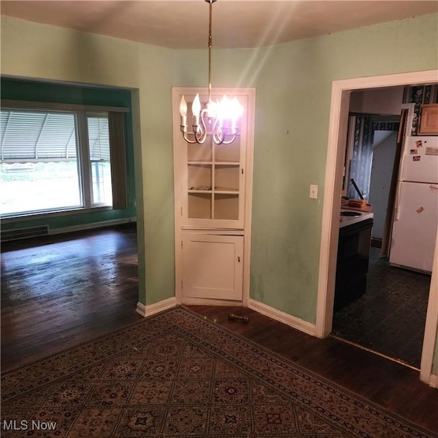 unfurnished dining area with a notable chandelier and dark wood-type flooring