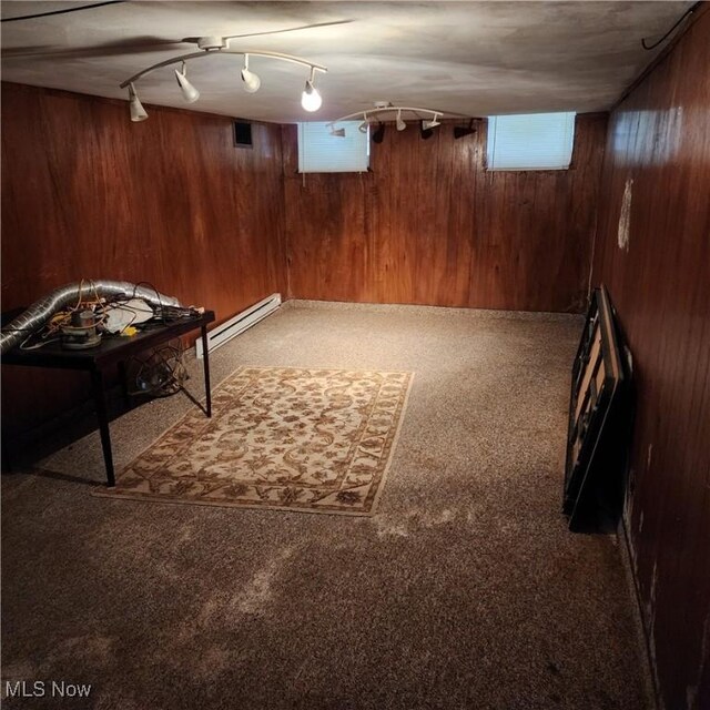 basement with carpet, a baseboard heating unit, wood walls, and track lighting