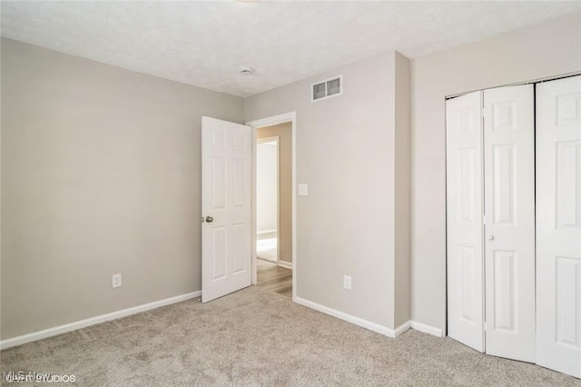 unfurnished bedroom with a textured ceiling, light colored carpet, and a closet