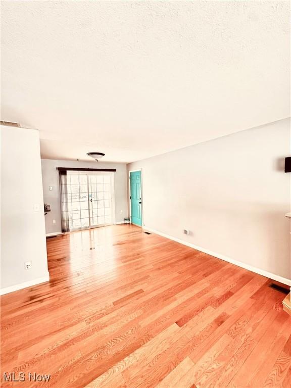 unfurnished living room featuring light wood-style flooring, baseboards, and a textured ceiling