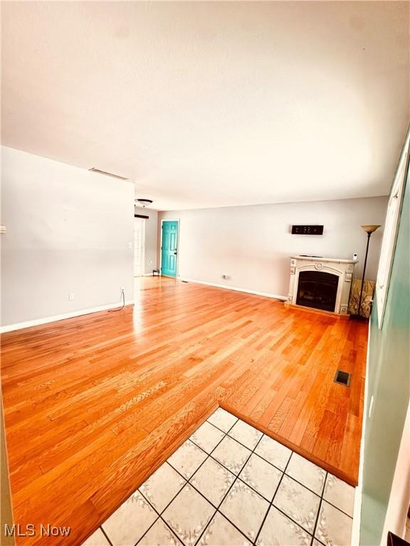 unfurnished living room with light wood-type flooring, visible vents, a fireplace, and baseboards