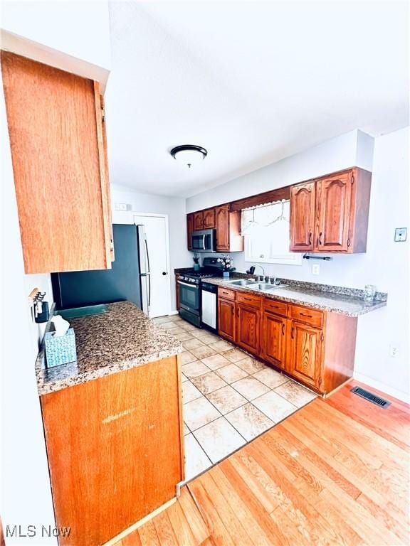 kitchen with light wood finished floors, visible vents, appliances with stainless steel finishes, brown cabinets, and a sink