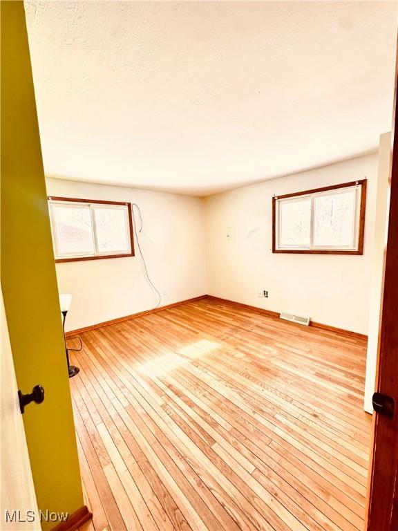 empty room with light wood-style floors and visible vents