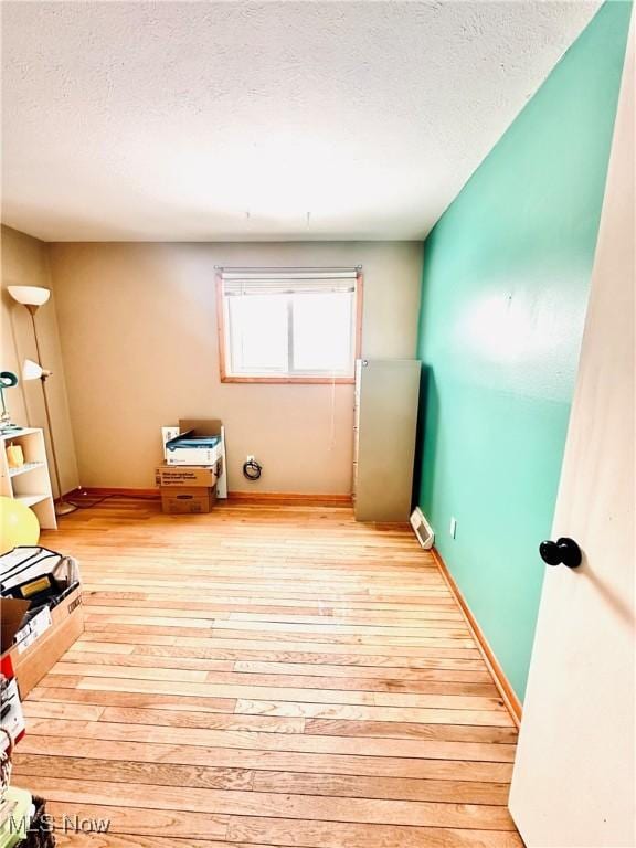 interior space featuring light wood-style floors, a textured ceiling, and baseboards