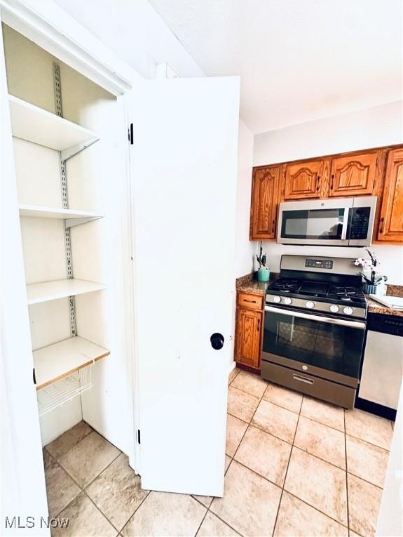 kitchen featuring appliances with stainless steel finishes, brown cabinetry, and light tile patterned flooring