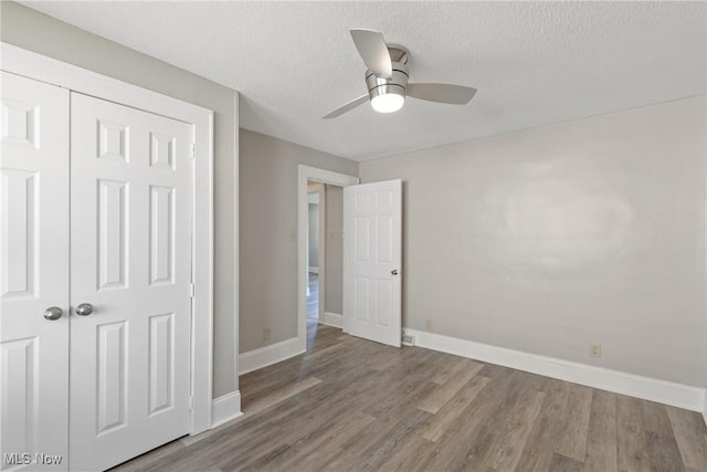 unfurnished bedroom with ceiling fan, a closet, wood-type flooring, and a textured ceiling