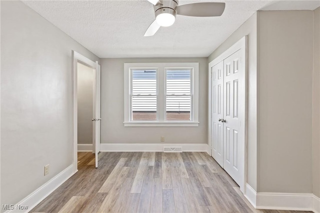 unfurnished bedroom with a textured ceiling, a closet, light hardwood / wood-style flooring, and ceiling fan