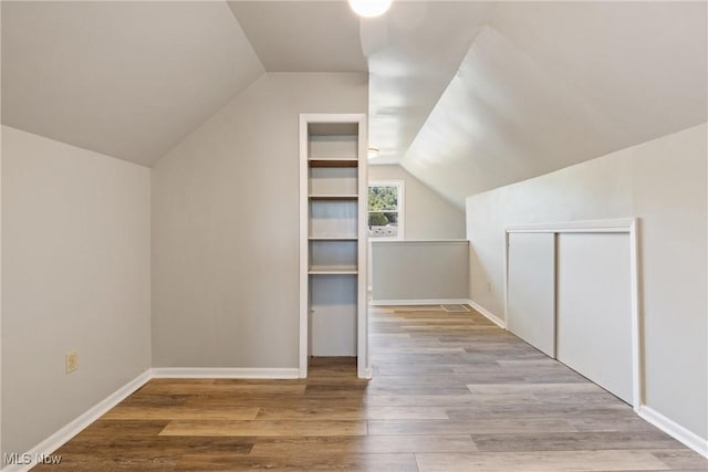 bonus room with light wood-type flooring and vaulted ceiling