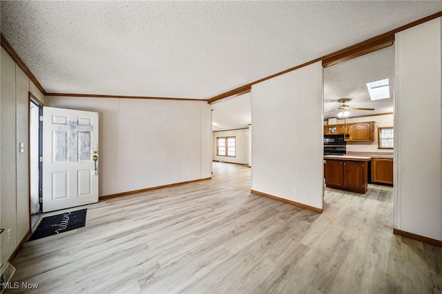 entrance foyer featuring ceiling fan, vaulted ceiling with skylight, ornamental molding, a textured ceiling, and light wood-type flooring