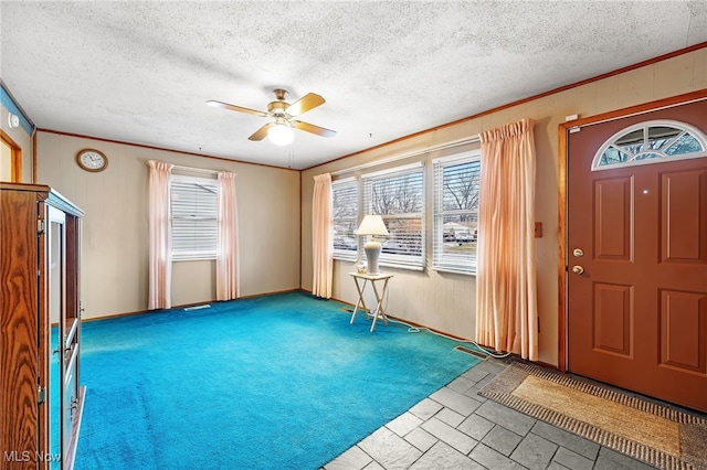 entryway featuring a textured ceiling, carpet floors, ceiling fan, and ornamental molding