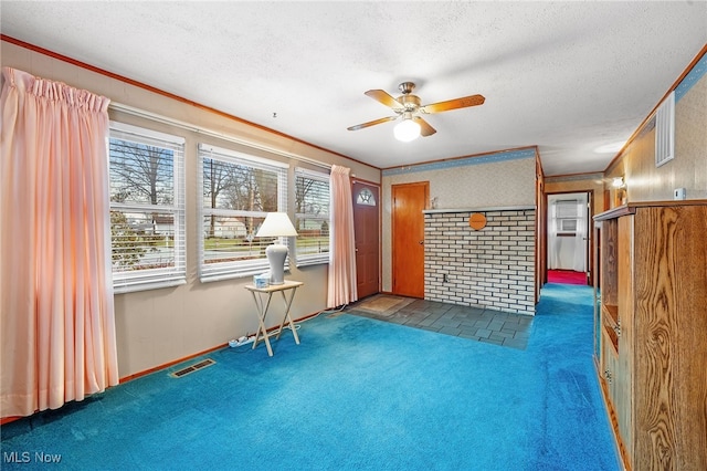 interior space with a textured ceiling, ceiling fan, wooden walls, crown molding, and dark colored carpet