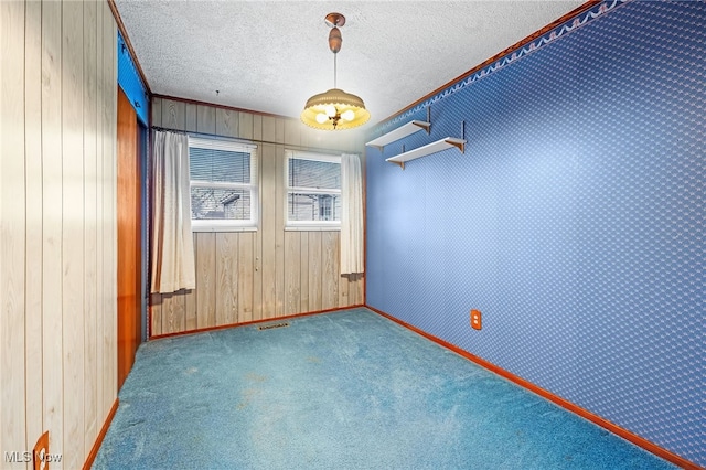 unfurnished room with carpet flooring, ornamental molding, a textured ceiling, and wooden walls