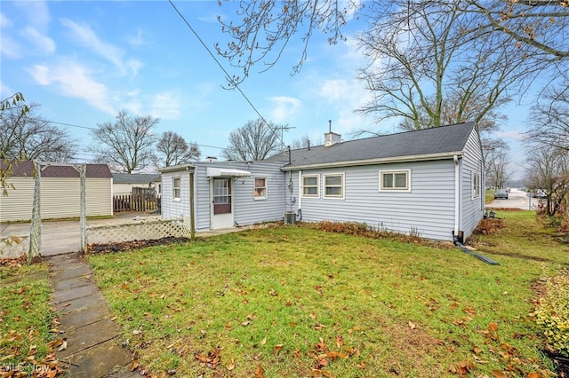 rear view of house with central AC unit and a lawn