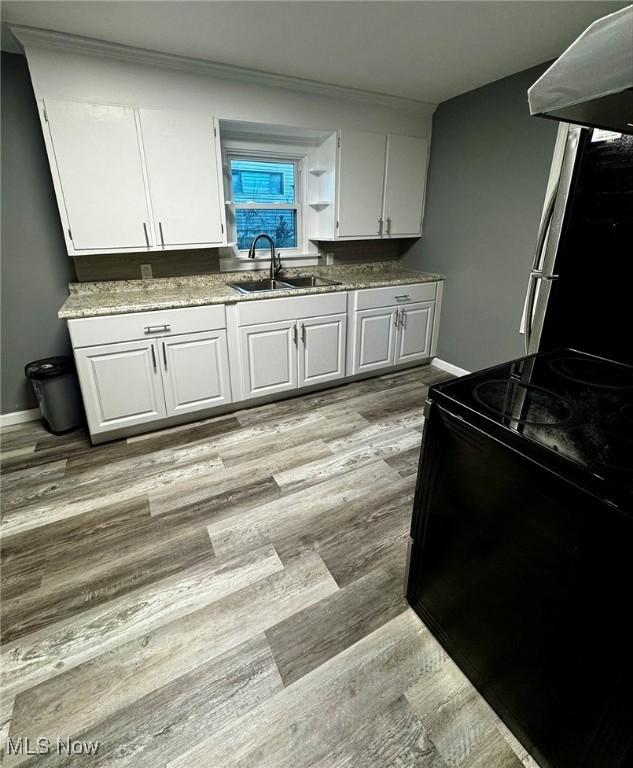 kitchen featuring black electric range oven, extractor fan, sink, light hardwood / wood-style flooring, and white cabinetry