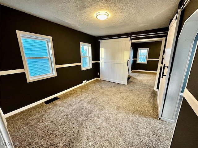 unfurnished bedroom with a barn door, carpet floors, and a textured ceiling