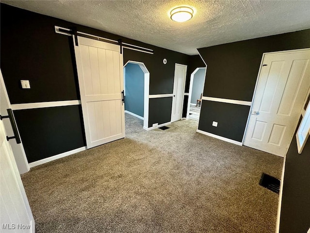 unfurnished bedroom featuring a textured ceiling, a barn door, and carpet floors