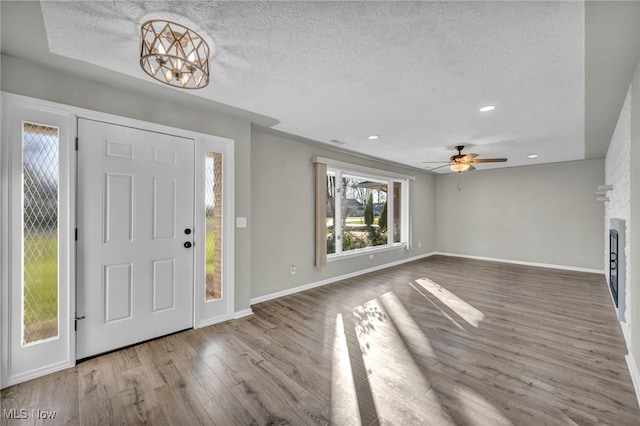 foyer featuring ceiling fan with notable chandelier, wood-type flooring, a textured ceiling, and a large fireplace