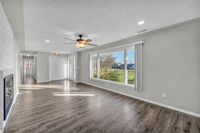 unfurnished living room with a textured ceiling, ceiling fan, a fireplace, and dark hardwood / wood-style floors