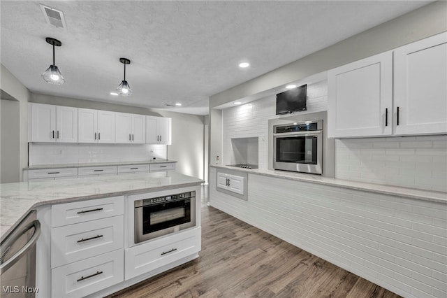 kitchen with stainless steel appliances, light stone counters, light hardwood / wood-style floors, decorative light fixtures, and white cabinets