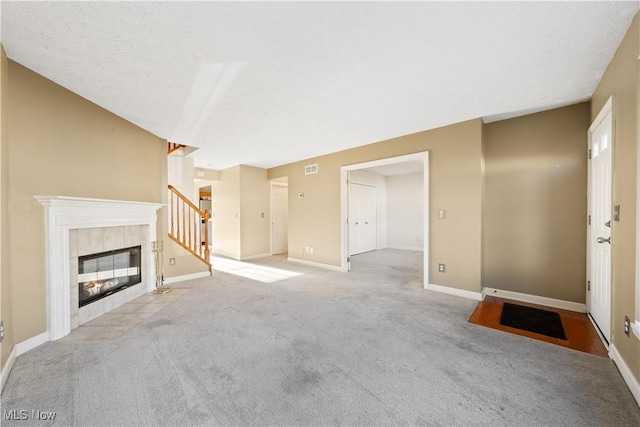 unfurnished living room featuring a tile fireplace, a textured ceiling, and light colored carpet