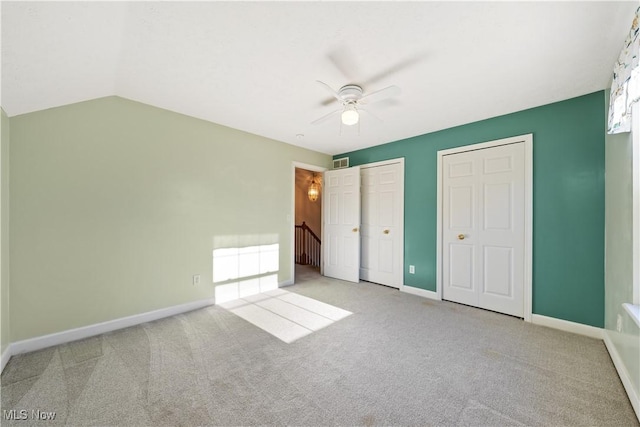 unfurnished bedroom with ceiling fan, light colored carpet, lofted ceiling, and two closets