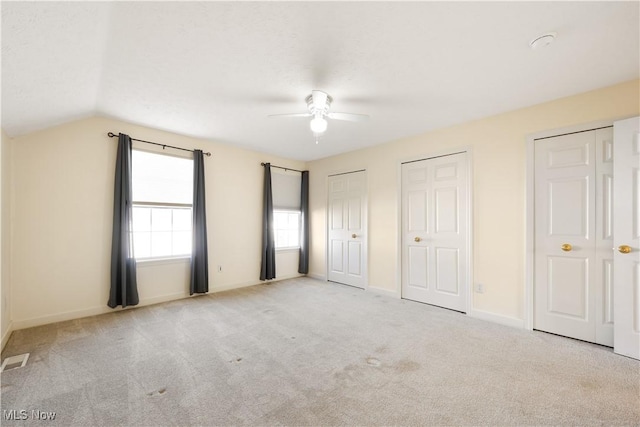 unfurnished bedroom with multiple closets, ceiling fan, light colored carpet, and vaulted ceiling