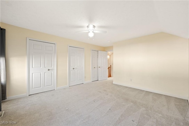 unfurnished bedroom featuring ceiling fan, vaulted ceiling, light colored carpet, and multiple closets