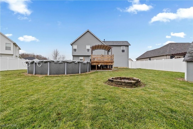 rear view of property with a swimming pool side deck, a yard, and a fire pit