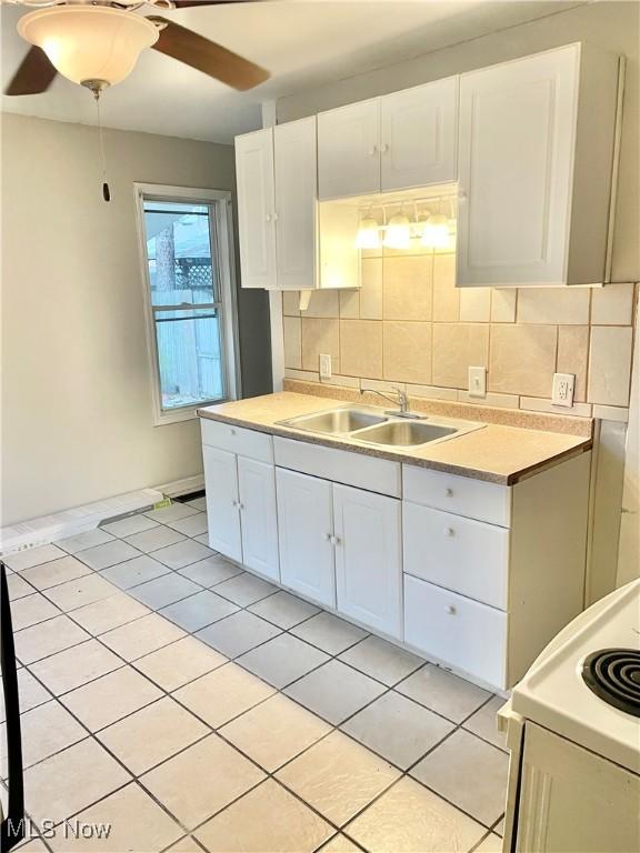 kitchen featuring decorative backsplash, ceiling fan, sink, white cabinets, and range