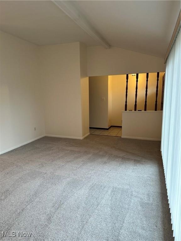 carpeted spare room featuring vaulted ceiling with beams