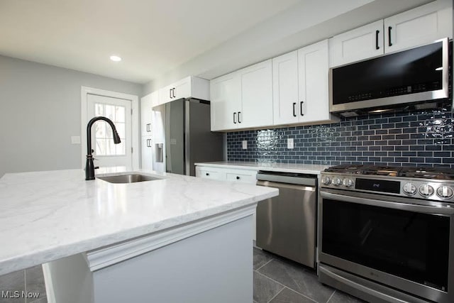 kitchen featuring a center island with sink, white cabinets, sink, light stone countertops, and stainless steel appliances