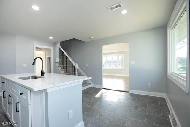 kitchen with white cabinetry, light stone counters, sink, and an island with sink