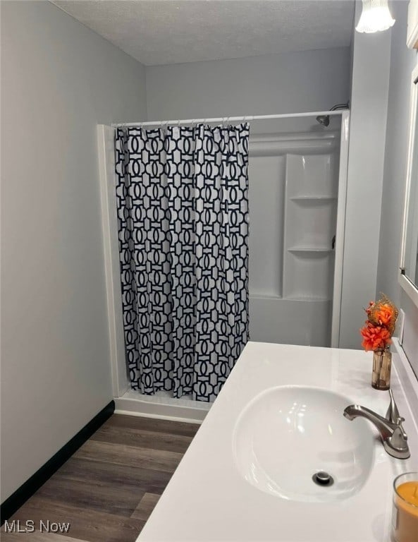 bathroom with hardwood / wood-style floors, a textured ceiling, curtained shower, and sink