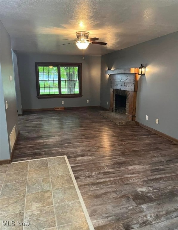 unfurnished living room with a textured ceiling, dark hardwood / wood-style floors, a stone fireplace, and ceiling fan