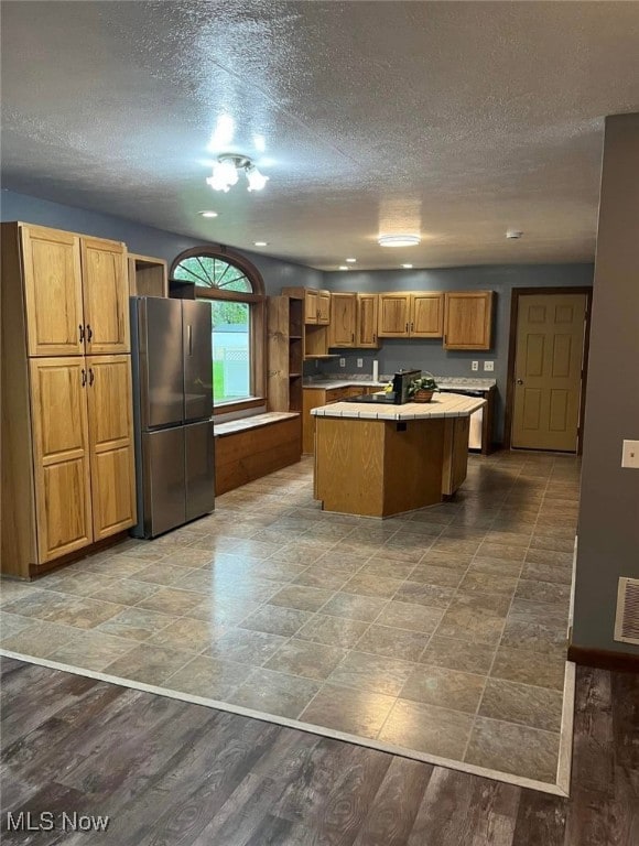 kitchen featuring dark hardwood / wood-style flooring, stainless steel fridge, a kitchen island, and a textured ceiling