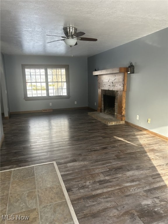 unfurnished living room with ceiling fan, dark hardwood / wood-style flooring, a textured ceiling, and a brick fireplace