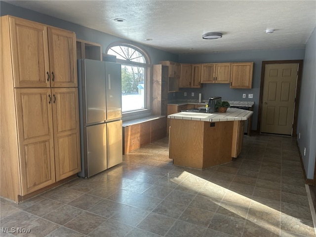 kitchen with tile counters, stainless steel fridge, a kitchen island, and a textured ceiling