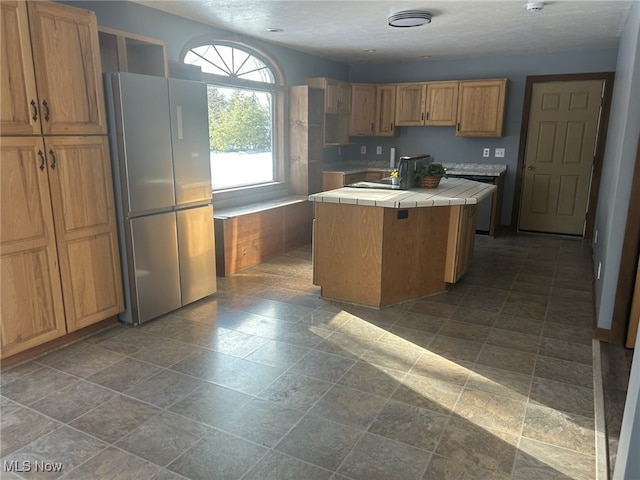 kitchen with stainless steel fridge, tile countertops, and a kitchen island