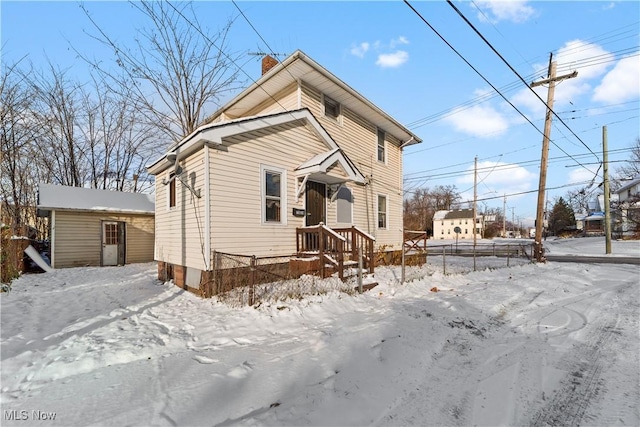 view of front of house featuring a chimney, fence, and an outbuilding