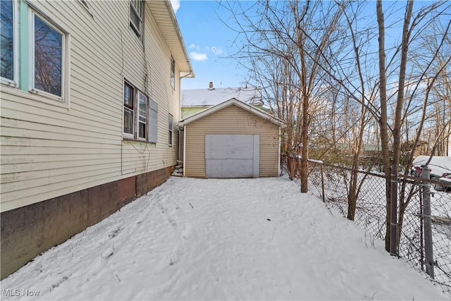 snowy yard featuring a garage, an outbuilding, fence, and a storage unit