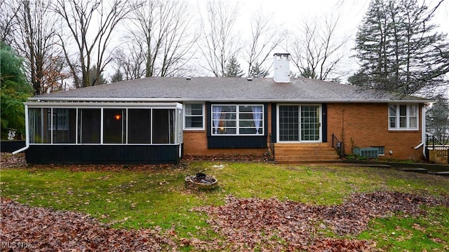 rear view of house with a sunroom, central air condition unit, an outdoor fire pit, and a lawn