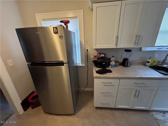 kitchen with stainless steel refrigerator, sink, white cabinets, and plenty of natural light