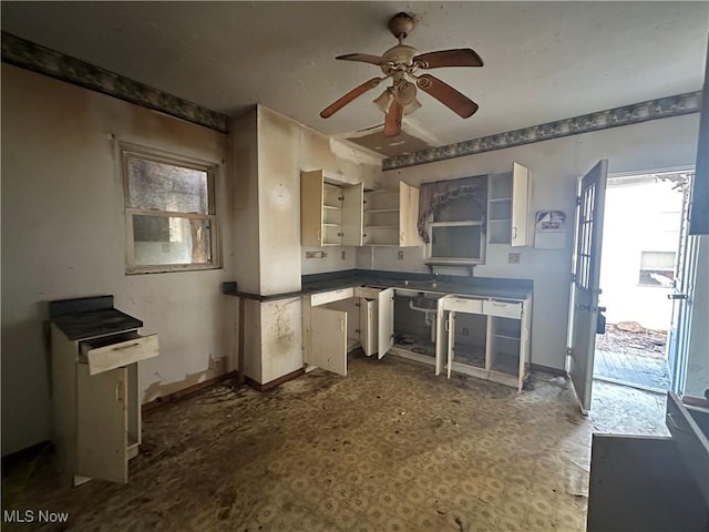 kitchen featuring dark countertops, a ceiling fan, white cabinetry, a sink, and baseboards