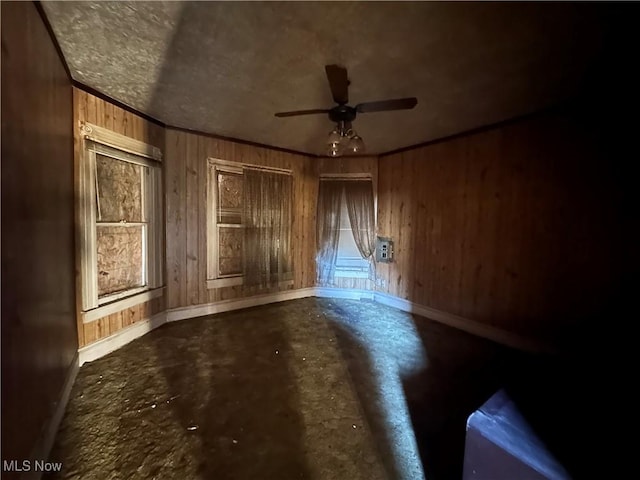 empty room featuring concrete floors, wooden walls, baseboards, and ornamental molding