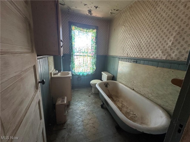 bathroom featuring toilet, a wainscoted wall, a freestanding bath, and wallpapered walls