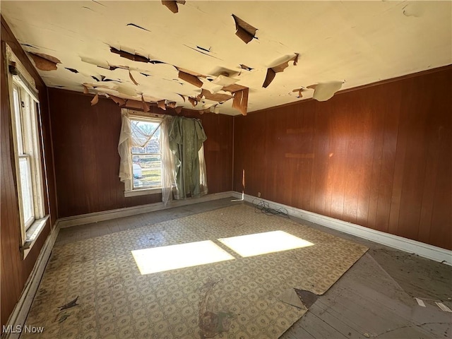 empty room featuring a baseboard heating unit, wooden walls, and baseboards