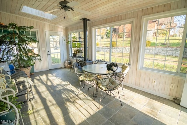 sunroom featuring a skylight, a wood stove, ceiling fan, and wooden ceiling