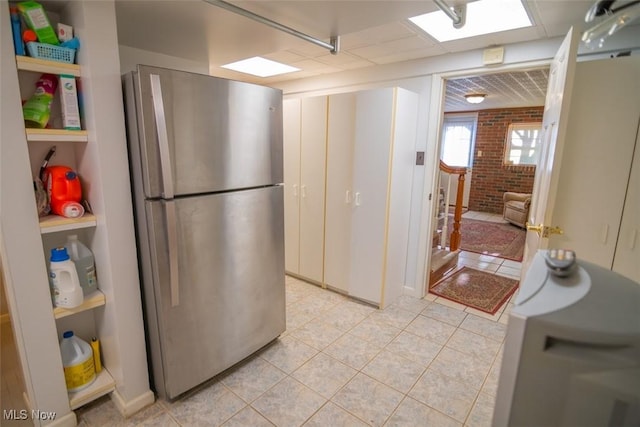 kitchen featuring stainless steel refrigerator, light tile patterned floors, and brick wall