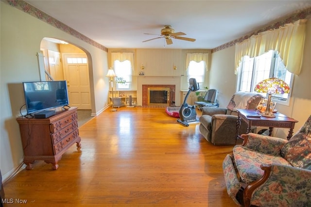 living room featuring light wood-type flooring, a brick fireplace, and ceiling fan