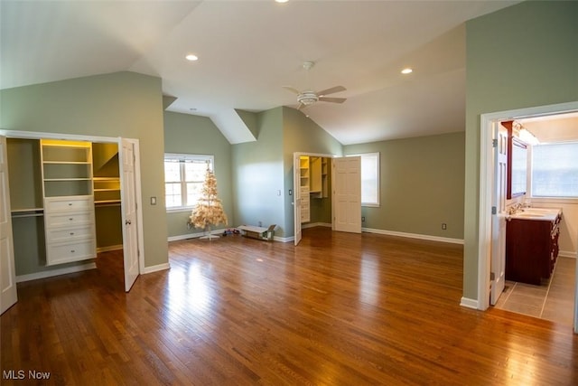 unfurnished bedroom featuring lofted ceiling, a walk in closet, ensuite bath, hardwood / wood-style flooring, and ceiling fan